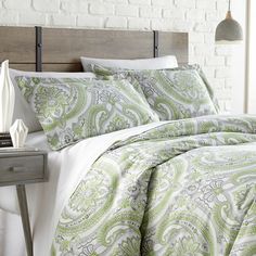 a bed with green and white bedspread next to a night stand in a bedroom