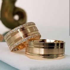 two gold wedding bands sitting on top of a white towel next to a green vase