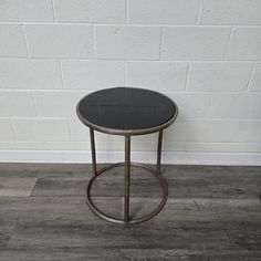 a small black table sitting on top of a hard wood floor next to a white brick wall