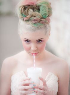 a woman with pink and green hair drinking from a cup while holding a straw in her hand