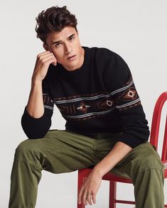 a young man is sitting on a red chair and posing for the camera with his hand under his chin