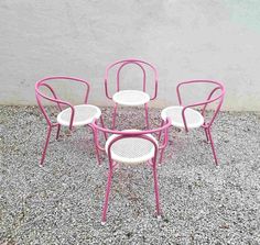 four pink and white chairs sitting on top of a gravel ground next to a wall