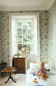 a baby sitting on top of a bed in a bedroom next to a dresser and window