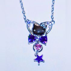 a hello kitty necklace with purple and pink crystals on it's side, hanging from a silver chain