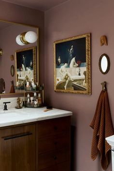 a bathroom with pink walls and two pictures on the wall above the sink, along with towels