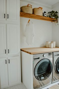 a washer and dryer in a white laundry room with open shelving on the wall