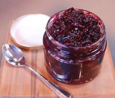 a wooden tray topped with a jar of jam next to a spoon