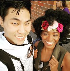 two people standing next to each other with flowers in their hair and one person smiling at the camera