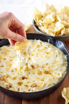 a hand dipping a tortilla chip into a skillet filled with cheese and chips