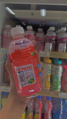 a person holding up a bottle of liquid in front of a shelf full of drinks