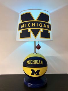 a michigan basketball lamp with the word michigan underneath it on a black table next to a white wall