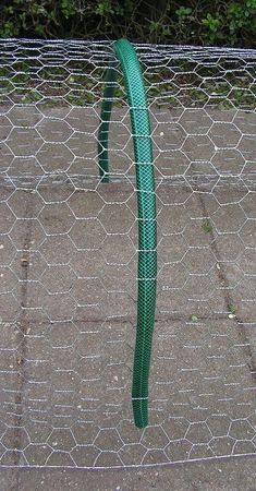 a close up of a wire fence with a green hose attached to it