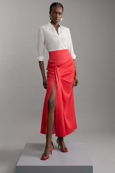 a woman in a white shirt and red skirt is standing on a gray platform with her legs crossed