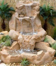 an image of a water fountain in the middle of a small garden with rocks and plants