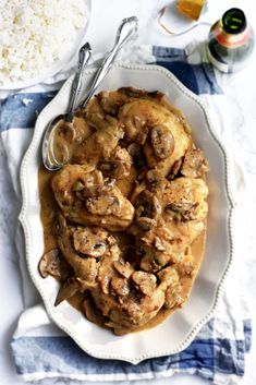 a white plate topped with meat covered in mushrooms and gravy next to rice