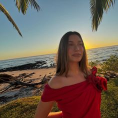 a woman in a red dress is standing on the beach at sunset with palm trees