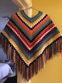 a multicolored crocheted shawl hanging on a wall next to a bed