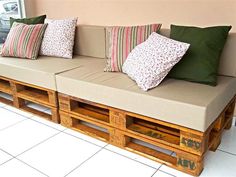 a couch made out of wooden pallets with pillows on top and bottom, sitting in front of a window