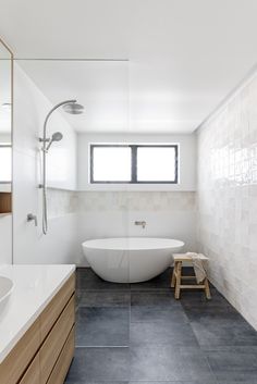 a large white bath tub sitting next to a bathroom sink under a window in a bathroom