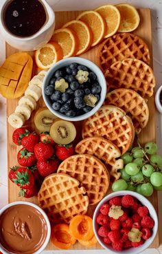 a wooden cutting board topped with waffles and fruit