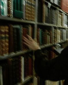 a person reaching for books on a book shelf in a library filled with lots of books