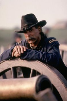 a man wearing a hat leaning on a wheel