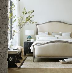 a bedroom with a bed, nightstands and a plant in the corner on the floor