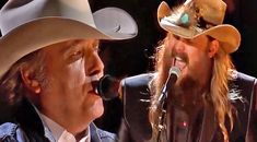 two men with long hair and hats on singing into microphones in front of each other