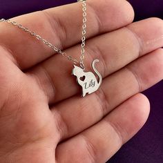 a hand holding a silver cat necklace with the word i love you on it's back