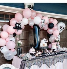 a table topped with lots of pink and white balloons next to a black cat balloon arch