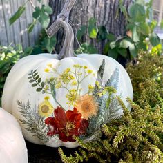 a painted pumpkin sitting on top of a wooden table next to some plants and flowers