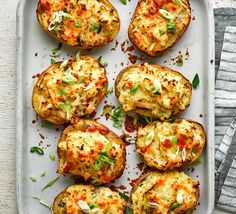 baked potatoes with cheese and seasoning on a white platter next to a napkin