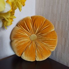 a round pillow sitting on top of a wooden table next to a vase with yellow flowers