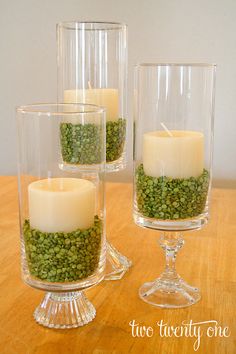 three clear glass vases filled with green moss and lit candles on a wooden table