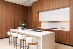 a kitchen with wooden cabinets and white counter tops, along with bar stools that are facing the sink