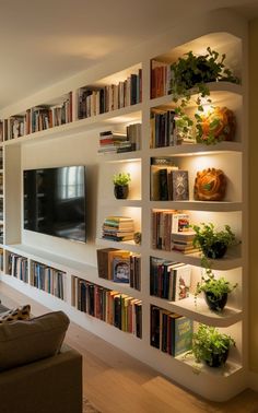 a living room filled with lots of books and plants on the wall next to a flat screen tv