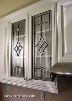 a kitchen with white cabinets and stained glass doors