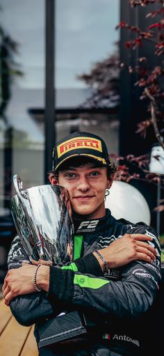 a man in a racing uniform is holding a trophy and posing for the camera with his arms crossed