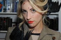 a woman with blonde hair wearing a jacket and red lipstick in front of bookshelves