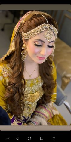 a woman with long hair wearing a yellow dress and gold jewelry on her head, sitting down