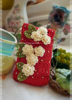 a crocheted cell phone case with flowers on it sitting next to other items