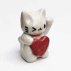 a white cat figurine holding a red heart