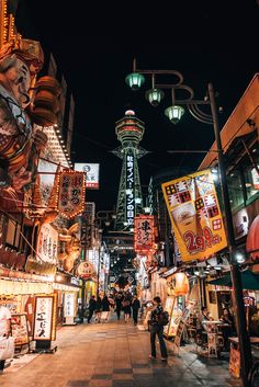 a city street at night filled with lots of shops and people walking around the area