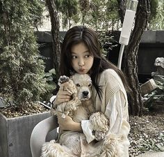 a woman is holding a dog in her lap and posing for the camera with trees behind her