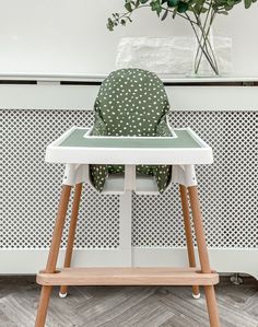 a green and white polka dot highchair in front of a wall with a plant