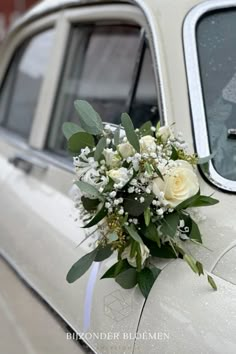 a bouquet of white flowers sitting on the side of a car with greenery and baby's breath