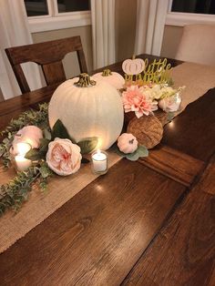 the table is set with candles and flowers on it, along with two pumpkins