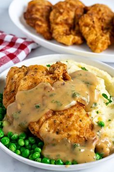 two plates filled with chicken and mashed potatoes covered in gravy next to green peas