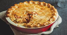 a pie sitting on top of a red dish next to a wine glass and napkin