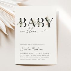 a baby is blooming card on top of a white table with flowers and greenery